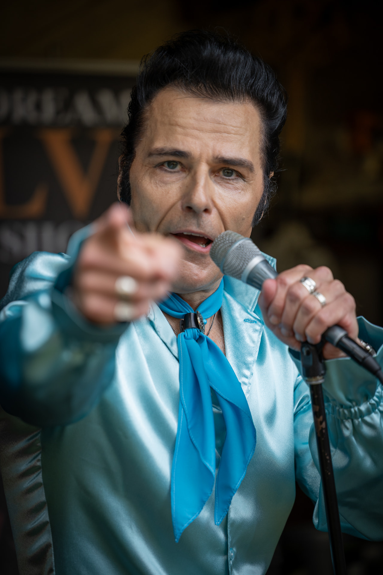 Elvis-esiintyjä osoittaa yleisöä kohti Dream Elvis Show -julisteen edessä
