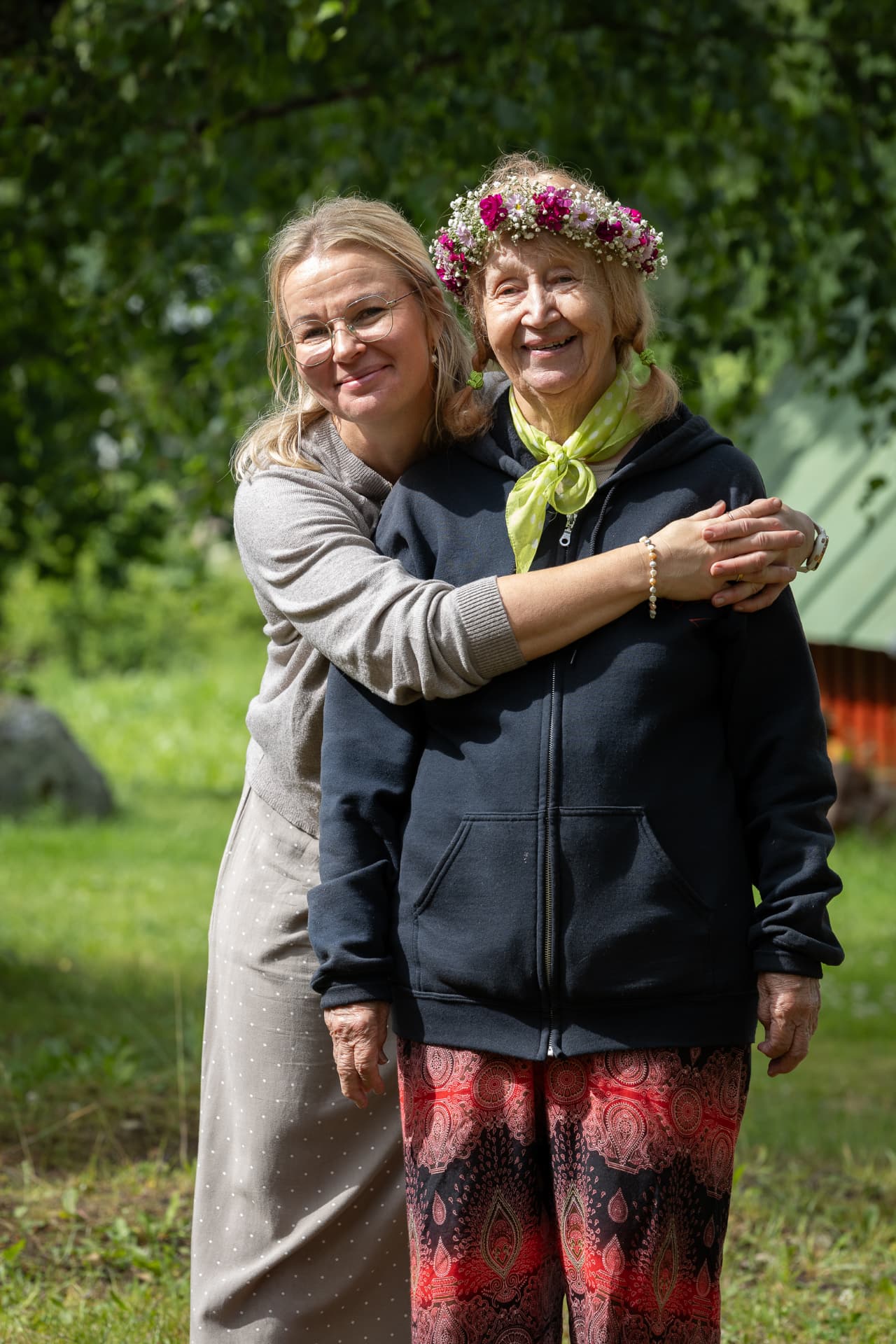 Marjatta kukkaseppele päässään halaamassa vierailijaa pihalla