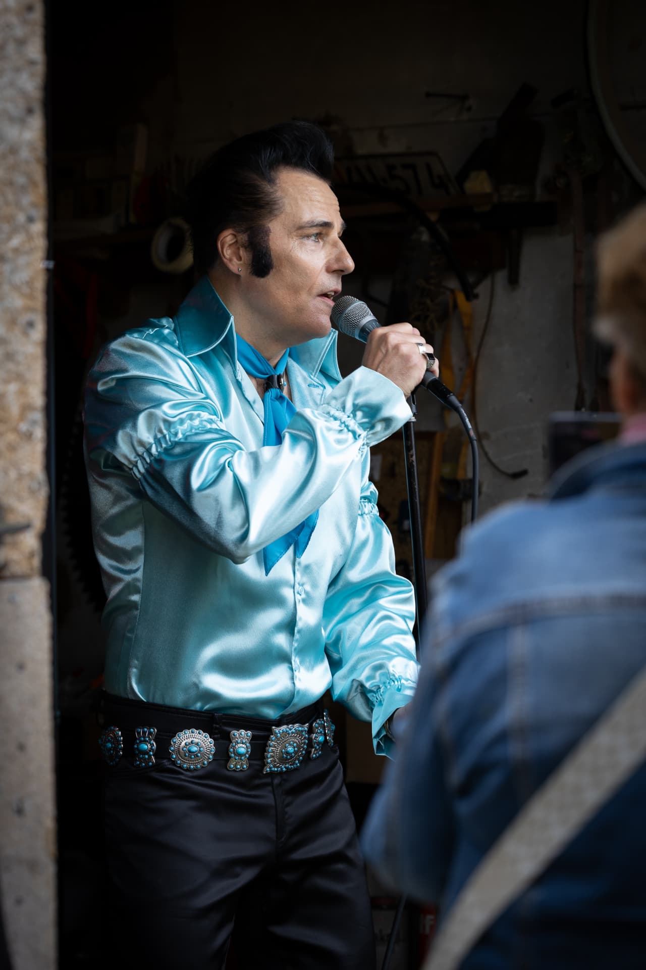 Elvis-esiintyjä turkoosissa satiinipaidassa laulaa mikrofoniin