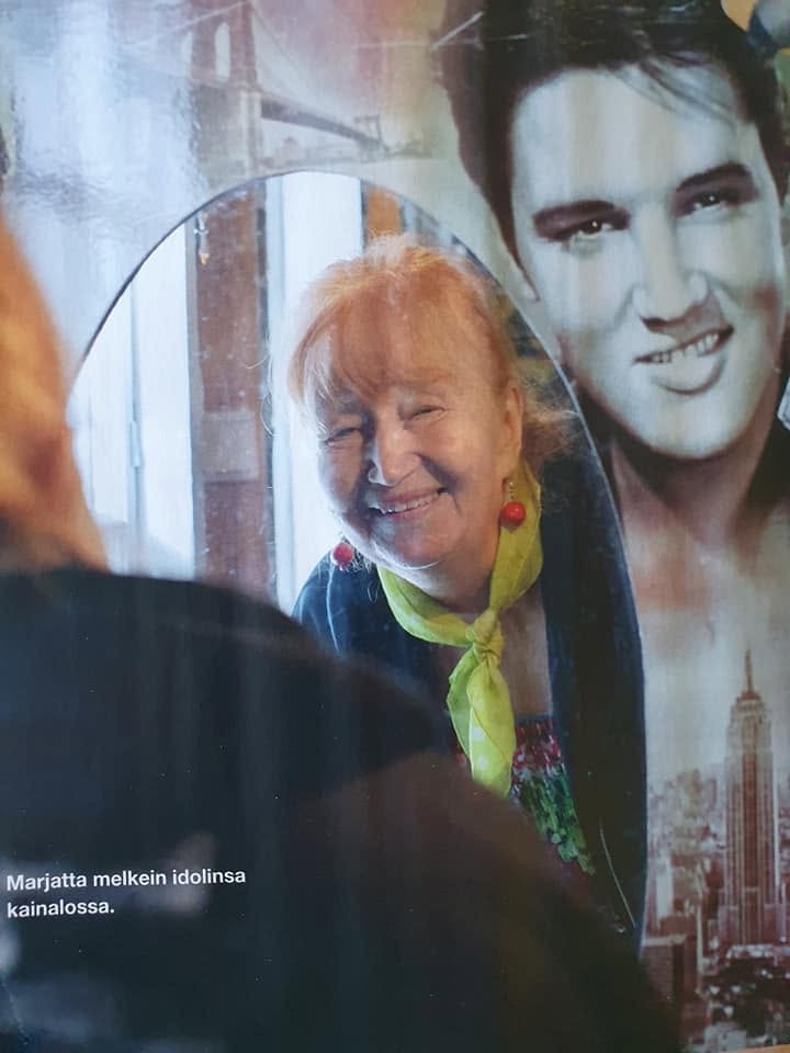 Marjatta hymyilee Elvis-julisteen edessä