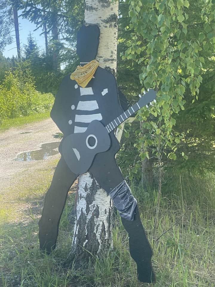Puinen Elvis-hahmo kitaran kanssa koivun juurella